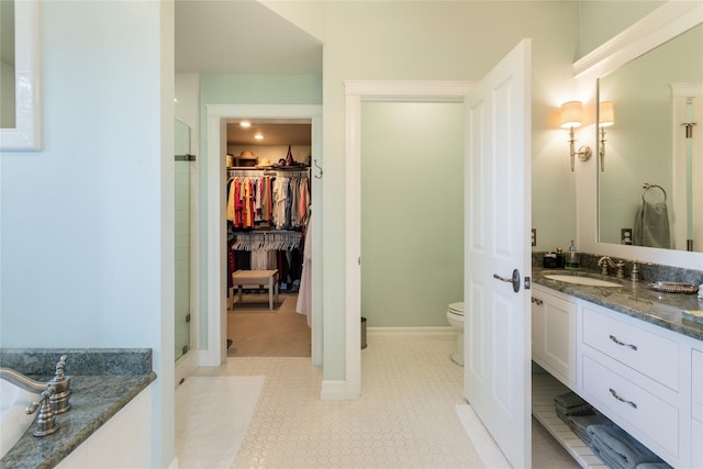 full bath with a walk in closet, toilet, a shower stall, baseboards, and vanity