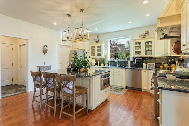 kitchen featuring glass insert cabinets, light wood-style floors, appliances with stainless steel finishes, a kitchen bar, and tasteful backsplash