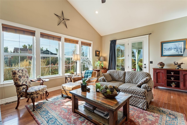 living area with a ceiling fan, visible vents, wood finished floors, baseboards, and high vaulted ceiling