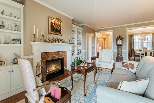 living room featuring a high end fireplace, built in shelves, crown molding, wood finished floors, and a notable chandelier