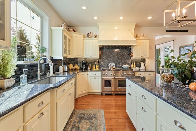 kitchen with light wood-type flooring, custom range hood, range with two ovens, an inviting chandelier, and a sink