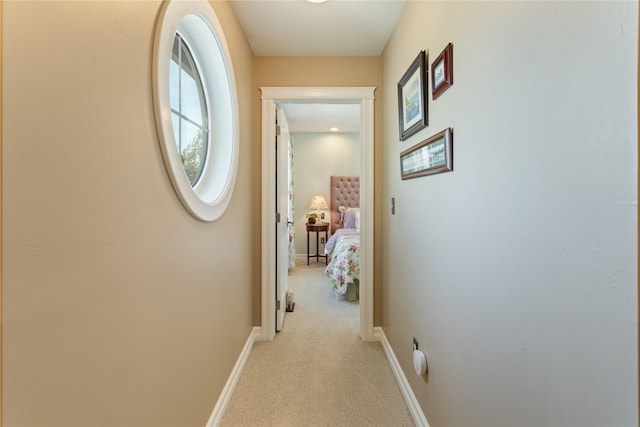 corridor featuring baseboards and light carpet