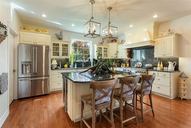 kitchen with glass insert cabinets, premium range hood, stainless steel fridge with ice dispenser, hardwood / wood-style flooring, and a sink