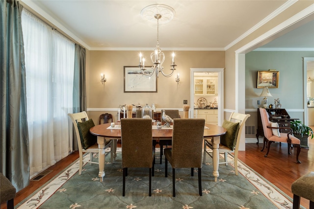 dining room with visible vents, wood finished floors, a chandelier, and ornamental molding