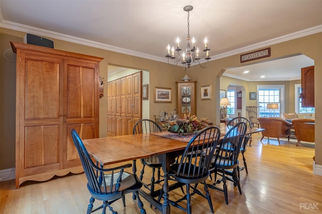 dining space with arched walkways, a chandelier, light wood finished floors, and ornamental molding