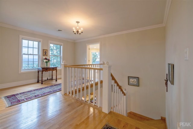 stairway with crown molding, a notable chandelier, wood finished floors, and plenty of natural light