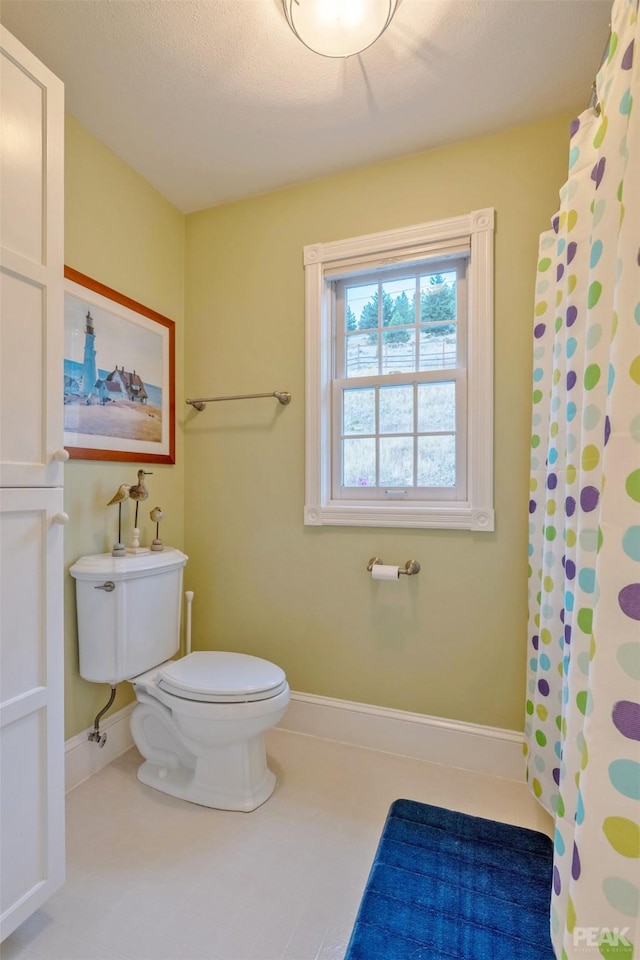 bathroom featuring a shower with shower curtain, toilet, baseboards, and tile patterned floors