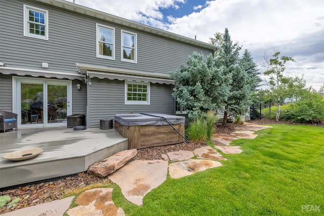 rear view of house featuring a wooden deck, fence, a yard, and a hot tub