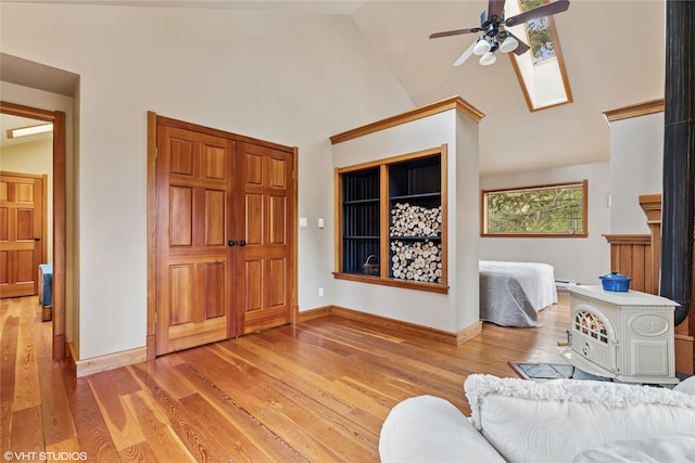 living area featuring a ceiling fan, baseboards, light wood finished floors, high vaulted ceiling, and a skylight