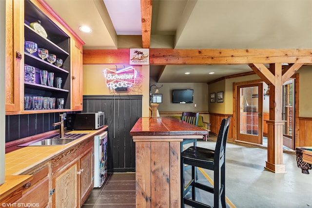 bar with stainless steel microwave, beamed ceiling, dishwashing machine, wainscoting, and a sink