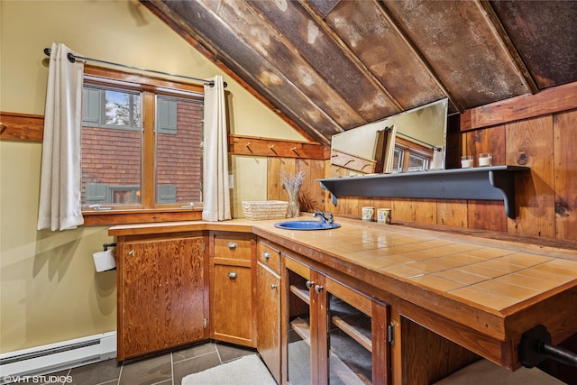 kitchen with lofted ceiling, a sink, tile counters, brown cabinets, and baseboard heating