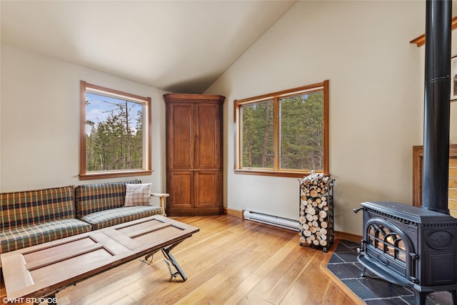 sitting room with light wood-style flooring, a baseboard heating unit, baseboards, lofted ceiling, and a wood stove