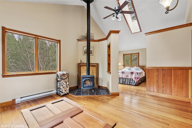 living area featuring a ceiling fan, high vaulted ceiling, a wood stove, wood-type flooring, and a baseboard heating unit