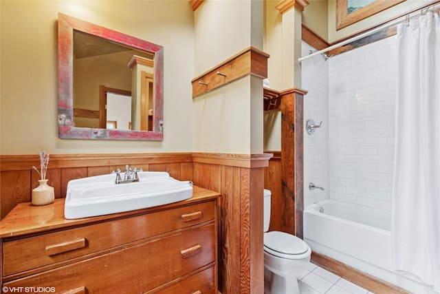 bathroom featuring tile patterned flooring, a wainscoted wall, toilet, shower / bath combination with curtain, and vanity