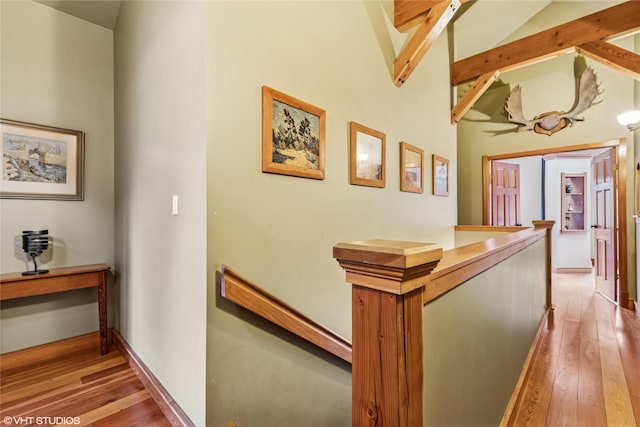 corridor with an upstairs landing, lofted ceiling with beams, baseboards, and hardwood / wood-style flooring