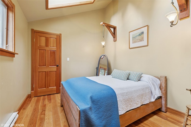 bedroom with light wood finished floors, baseboard heating, baseboards, and lofted ceiling