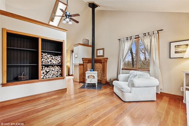 living area with a ceiling fan, baseboards, high vaulted ceiling, a wood stove, and wood-type flooring