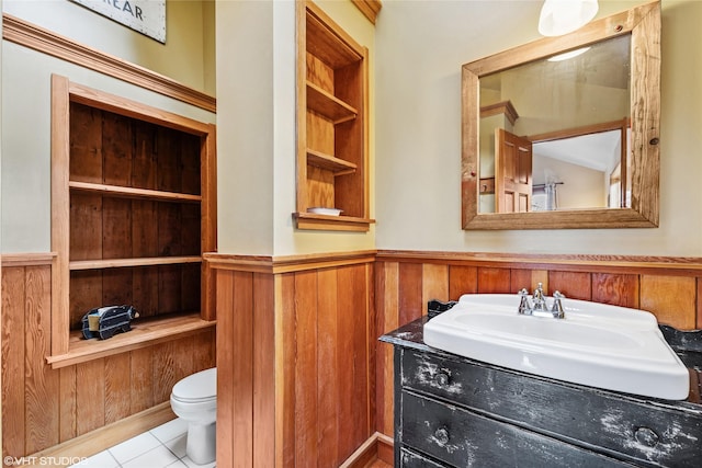 bathroom featuring wooden walls, toilet, wainscoting, tile patterned floors, and vanity