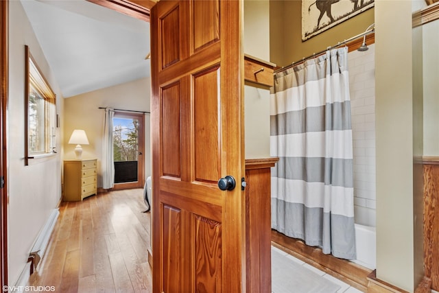 bathroom with shower / tub combo with curtain, wood-type flooring, baseboards, and vaulted ceiling