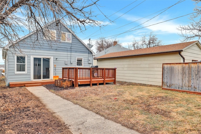 rear view of house with a lawn, a deck, and fence