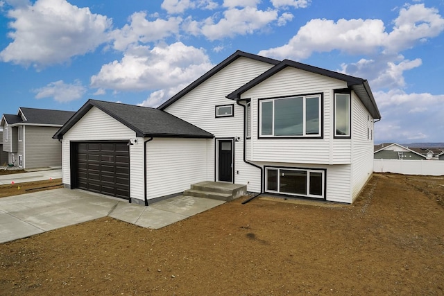 split level home with concrete driveway, an attached garage, and fence