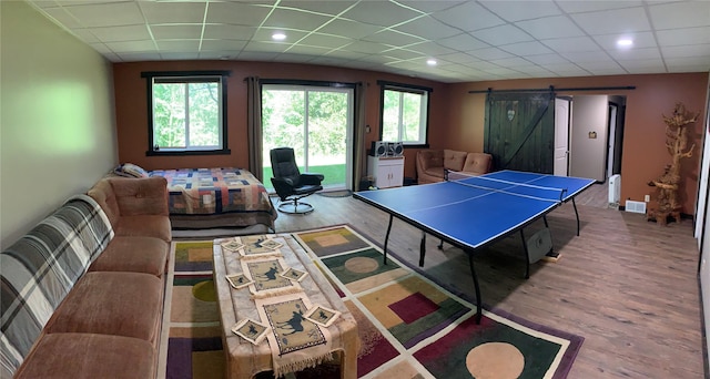 game room featuring a paneled ceiling, a barn door, plenty of natural light, and wood finished floors