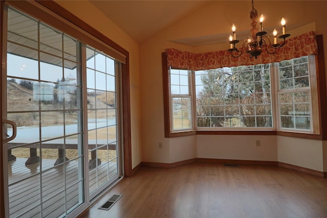 unfurnished dining area featuring visible vents, a chandelier, lofted ceiling, wood finished floors, and plenty of natural light