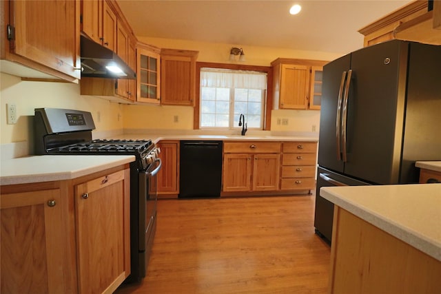 kitchen featuring under cabinet range hood, light wood-type flooring, light countertops, appliances with stainless steel finishes, and a sink