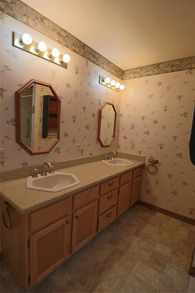 full bath featuring a sink, baseboards, double vanity, and wallpapered walls