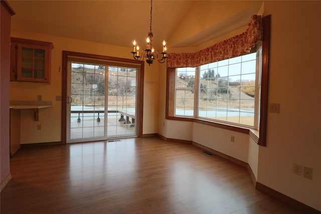 unfurnished dining area featuring baseboards, an inviting chandelier, and wood finished floors