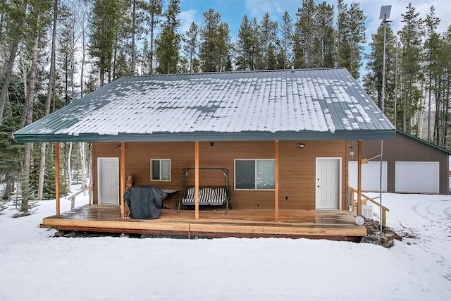 snow covered property with metal roof, a garage, a wooden deck, and an outdoor structure