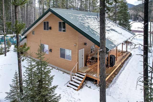 snow covered property featuring a wooden deck, stairs, and metal roof