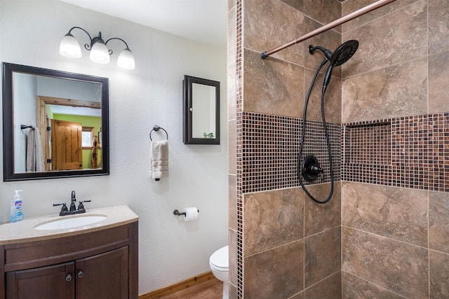 full bath with a tile shower, toilet, vanity, and wood finished floors