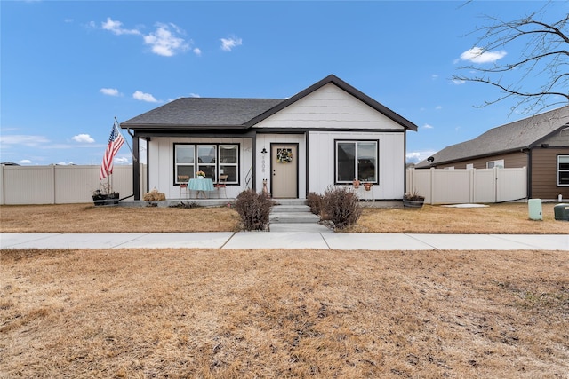 view of front of property featuring a front lawn, fence, board and batten siding, and roof with shingles