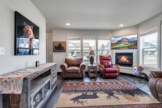 living area featuring recessed lighting, a textured ceiling, a glass covered fireplace, and dark wood-style flooring