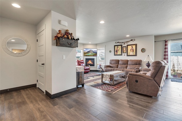 living room featuring a textured ceiling, dark wood-style floors, recessed lighting, a lit fireplace, and baseboards