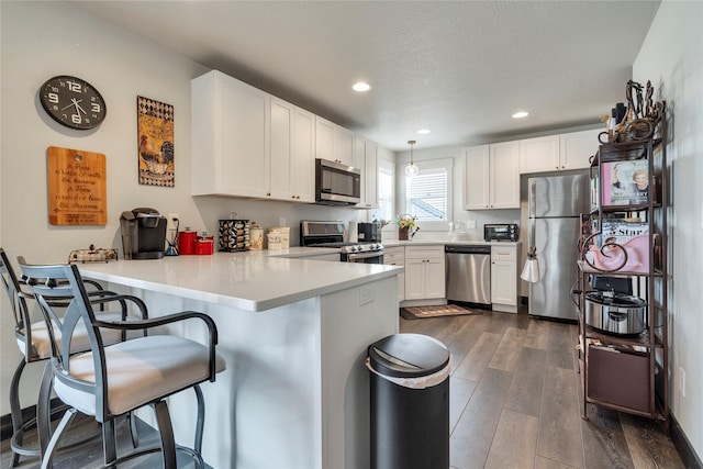 kitchen featuring a kitchen bar, a peninsula, stainless steel appliances, white cabinetry, and dark wood-style flooring