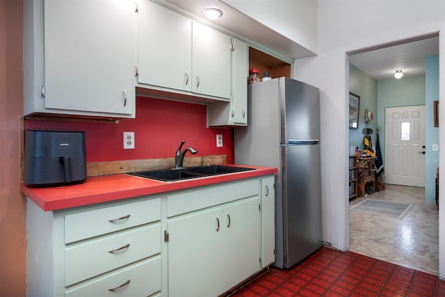 kitchen featuring light countertops, freestanding refrigerator, dark floors, and a sink