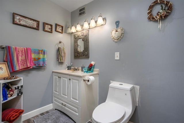 half bathroom featuring visible vents, toilet, wood finished floors, baseboards, and vanity