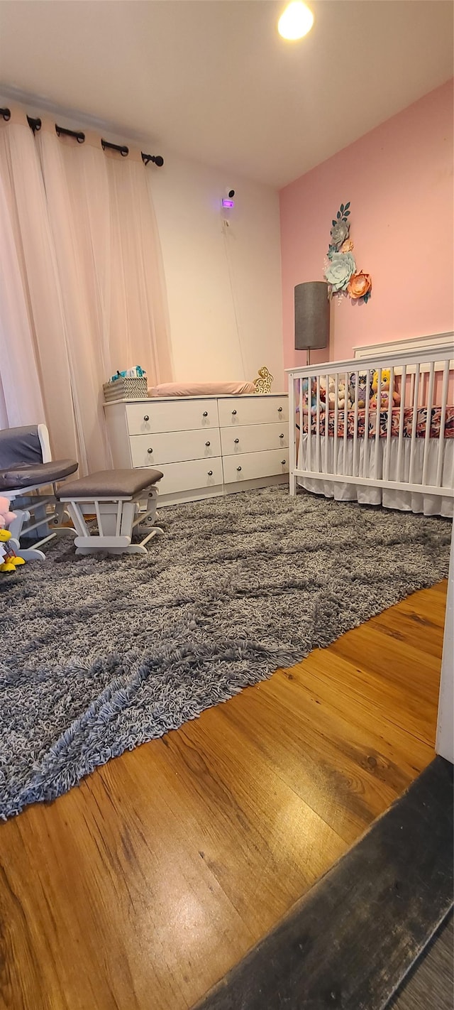 bedroom featuring a crib, baseboards, wood finished floors, and a barn door