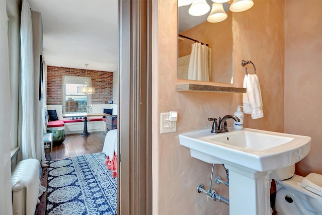 full bath with radiator, brick wall, a sink, hardwood / wood-style flooring, and toilet