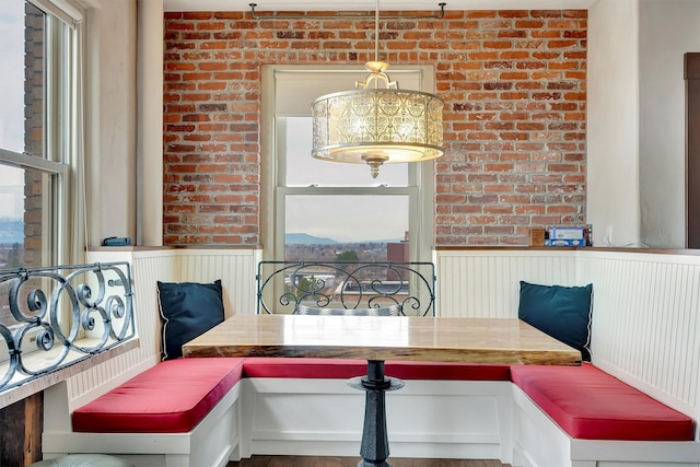 dining space featuring breakfast area, a wainscoted wall, and brick wall