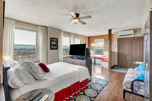 bedroom with multiple windows, brick wall, a wall mounted air conditioner, and hardwood / wood-style floors