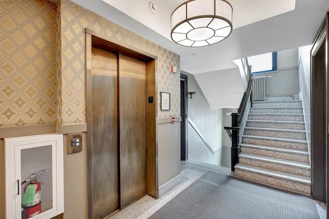 stairway with elevator, a wainscoted wall, wallpapered walls, and carpet