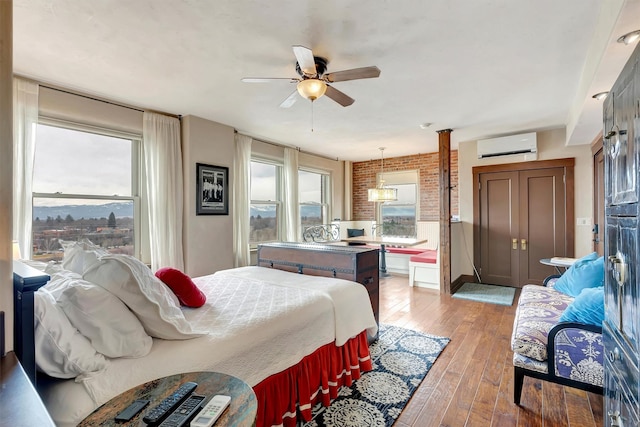 bedroom with a wall mounted air conditioner, brick wall, ceiling fan, and light wood finished floors