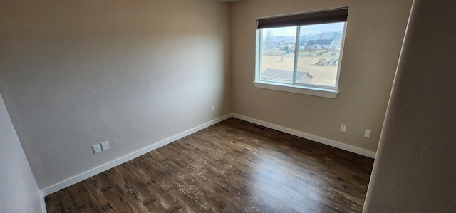 unfurnished room with dark wood-type flooring, visible vents, and baseboards