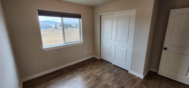 unfurnished bedroom featuring a closet, baseboards, visible vents, and dark wood-style floors