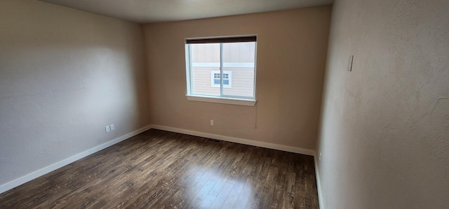 empty room with baseboards, hardwood / wood-style floors, and a textured wall