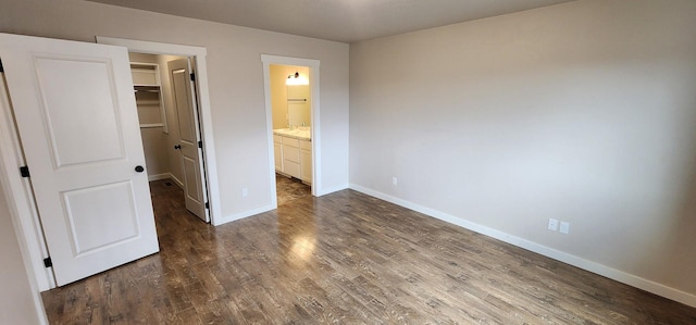 unfurnished bedroom with dark wood-style floors, a closet, a walk in closet, and baseboards