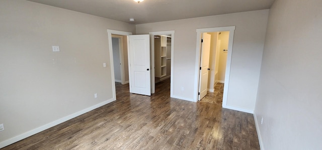 unfurnished bedroom featuring a closet, a walk in closet, baseboards, and wood finished floors